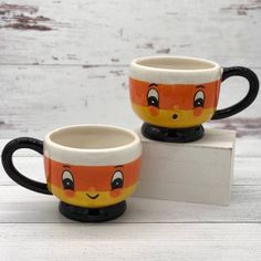 two mugs with faces painted on them are sitting on a white surface and one is black