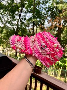 a woman's hand is holding up a pink knitted hat with pearls on it