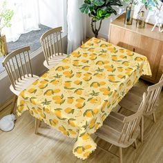 a dining room table covered with a yellow lemon print cloth next to two chairs and a potted plant