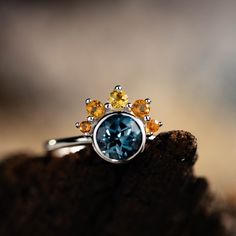 a blue ring with yellow and orange stones on it sitting on top of a piece of wood