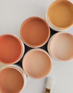 four paint cans with different shades of oranges and yellows next to a brush