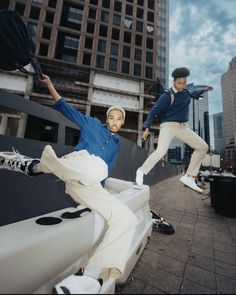 two young men jumping in the air on top of a white structure with buildings in the background