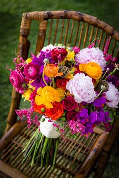 a bouquet of colorful flowers sitting on top of a wooden chair in the middle of a field