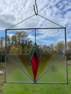 a stained glass sun catcher hanging from a chain on a grassy field with trees in the background