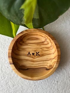 a wooden bowl with the word ak engraved on it next to a green leafy plant