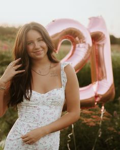 a beautiful young woman standing in front of a large pink number 20 sign with her hand on her hip