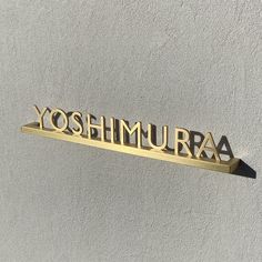 the word yoshimura spelled in gold metal letters on a white wall with shadows