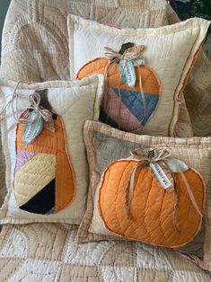 three decorative pumpkin pillows on a quilted bedspread with tags attached to them