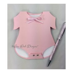 a pink baby bodysuit and pen on a table