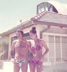 two people in bathing suits standing next to each other near a building with a roof