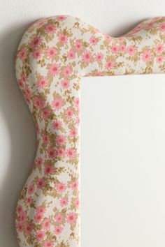 a mirror with pink flowers on it next to a white wall and a wooden frame