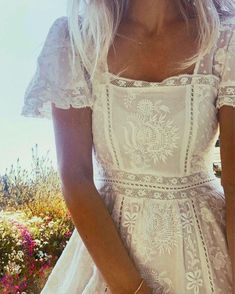 a woman in a white dress is standing near some flowers and holding her hand on her hip