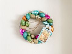 a wreath made out of eggs and other colorful beads on a white wall with a photo hanging from the front