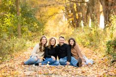 three people are sitting on the ground in front of trees and leaves, posing for a family photo