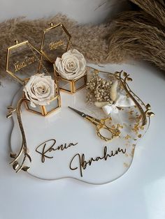 two white roses sitting on top of a table next to some gold and silver items