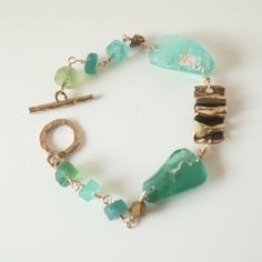 Are you looking for a unique piece of jewelry that tells a story and is one-of-a-kind? This beautiful handcrafted bracelet is made from Ancient Roman glass, bronzed crystals and a bronze toggle clasp. The genuine glass is  intricately shaped in stunning shades of blues and greens. Roman glass comes from raw glass found in Israel, Egypt and Lebanon.  The glass came from ancient jars, wine goblets or vessels and was buried for thousands of years in sand  which gives it iridescence and its gorgeous color. The bronze colored crystals and wavy bronze spacer add to the unique design and beauty of this special piece of history. Roman Glass Jewelry, Ancient Roman Glass, Unique Jewelry Gifts, Roman Glass, Handcrafted Bracelets, Wine Goblets, Plastic Jewelry, Glass Bracelet, Ancient Romans