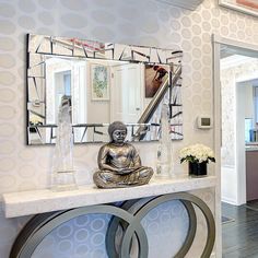 a buddha statue sitting on top of a white counter next to a mirror and vase