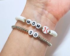 Baseball Mom Clay Bead Bracelet | Personalizable Heishi Baseball Mom Stretch Bracelet | Stackable Bracelets Gift for Her IMPORTANT NOTE: This listing is for a single bracelet or up to 2 bracelets depending on option selection. Details: Handmade Item Bracelet Length: See Size Chart in Images Materials: 4mm silver or gold plated beads (tarnish resistant), plastic letter beads, baseball charm bead Closure: Tie Made to Order Personalization: Bead Colors: See color chart in images Accent Bead Colors: Gold plated, silver plated, or rose gold plated  "mom" phrasing: indicate in personalization box for variations such as "mama." If no specification in personalization box, MOM will be used as default. ✨ Please measure your wrist before ordering as we do not offer returns or exchanges for resizing. Baseball Mom Bracelet Stack, Adjustable Stackable White Charm Bracelet, Personalized White Beaded Bangle Bracelet, White Bracelets For Mother's Day Jewelry Making, White Bracelets For Jewelry Making And Mother's Day, Silver Beaded Wristband For Gifts, Silver Beaded Wristband As Gift, White Stackable Charm Bracelet With Round Beads, Customized Adjustable Silver Beaded Bracelets