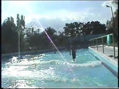 two people are walking in the water at an outdoor swimming pool while another person watches