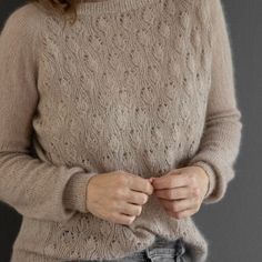 a woman wearing a sweater and jeans with her hands in her pockets, standing against a gray background