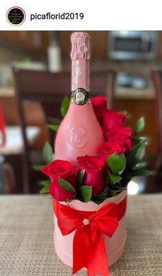 a pink bottle with roses in it sitting on a table next to a red ribbon