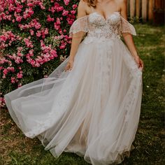 a woman in a wedding dress posing for the camera with pink flowers behind her,