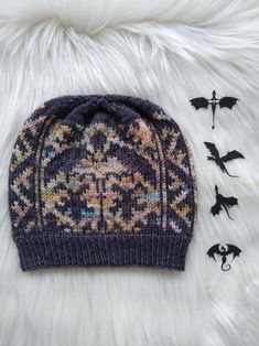 a knitted beanie hat with bat decorations on the side and two bats laying next to it