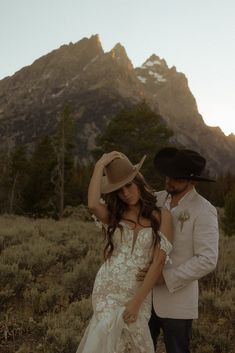 a man and woman standing next to each other in a field with mountains behind them