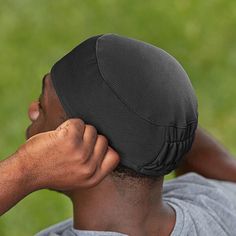 a man wearing a black hat covering his face with one hand while sitting in the grass