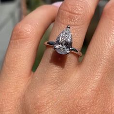 a woman's hand holding an engagement ring with a pear shaped diamond on it