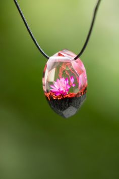 a glass ball with pink flowers in it hanging from a black cord on a green background