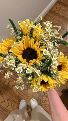 a bouquet of sunflowers and daisies in someone's hand on the floor