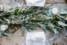 the table is set with candles, napkins and greenery