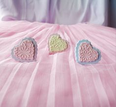 three small heart shaped cookies sitting on top of a pink bed sheet with white trim