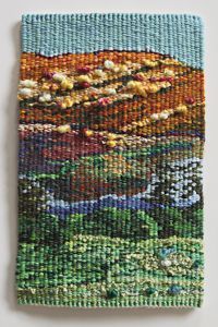 a small square beaded painting with mountains in the background