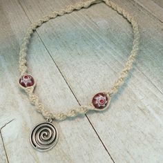 a necklace with two red glass beads and a silver spiral charm on a rope bracelet