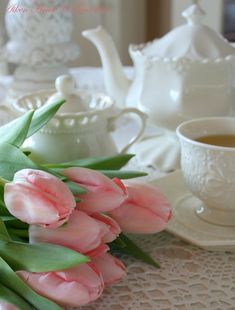 pink tulips are sitting on a table next to a cup of tea and saucer