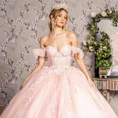 a woman in a pink ball gown standing next to a wall with flowers on it