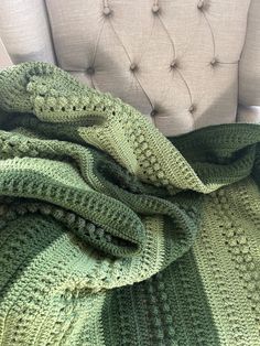 a green crocheted blanket sitting on top of a white chair next to a pillow