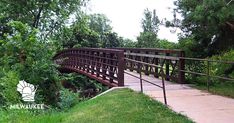 a wooden bridge over a small stream in a park with green grass and trees on both sides