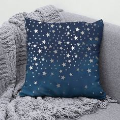 a blue pillow with silver stars on it sitting on a gray couch next to a blanket