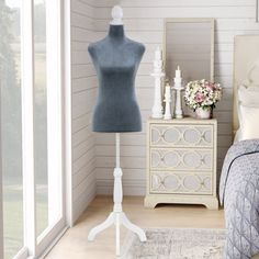 a mannequin is standing next to a bed in a room with white walls