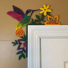 a colorful metal humming bird sitting on top of a white door frame next to a wall