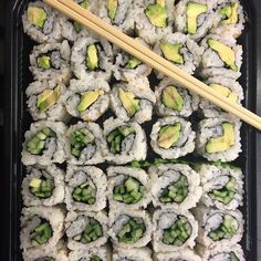 sushi rolls and chopsticks in a black tray with green vegetables on top