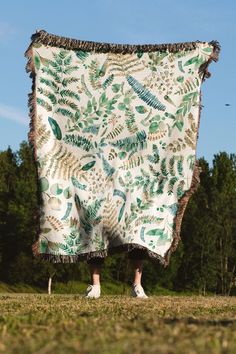 a person is holding up a blanket with leaves on it in front of some trees