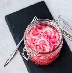 a jar filled with red onions sitting on top of a black napkin next to a fork