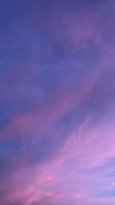 an airplane is flying high in the sky at sunset or dawn with pink and blue clouds