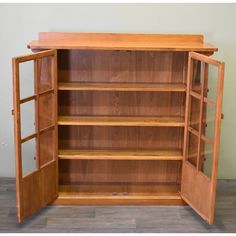 an open wooden bookcase with doors and shelves on the front, in a room with hard wood flooring