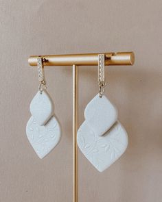 two white square shaped earrings hanging from a wooden hanger