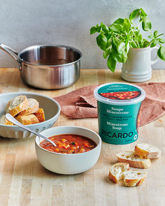 soup, bread and vegetables on a table with a pot of basil in the background